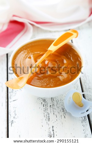 Baby food in bowl with spoon on white wooden background