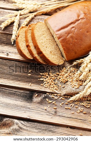 Ears of wheat with wheat grains and bread on brown wooden background