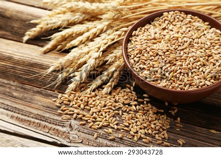 Ears of wheat and bowl of wheat grains on brown wooden background