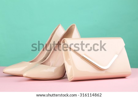 Pair of beige women\'s high-heeled shoes with handbag on a pink background