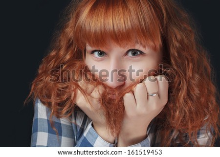 frightened red-haired girl hides her face in her hair on a dark background