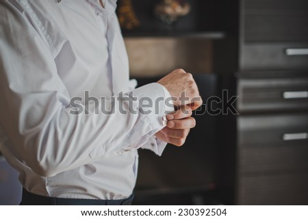 Hands of the young man clasping cuff links on shirt cuffs.
