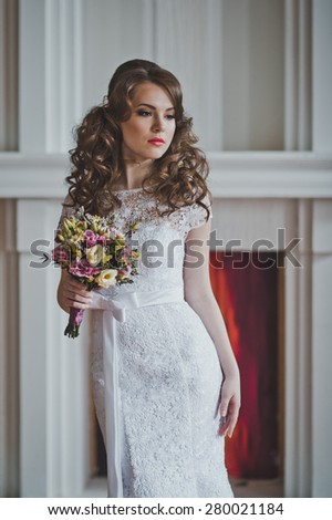 The girl with a bunch of flowers in a wedding dress costs at a fireplace.
