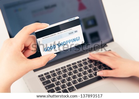Woman\'s hand holding a bank card over a laptop. On the card is written \