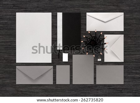 Top view of template for corporate branding identity for design presentation or portfolio on black table. Mockup includes paper, envelopes, business card, notebook, pencils, eraser, binder clip.