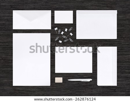 Top view of branding identity mockup with different paper templates for design presentation or portfolio on black table. Includes envelopes, sheets, business card, pen, eraser, clips.