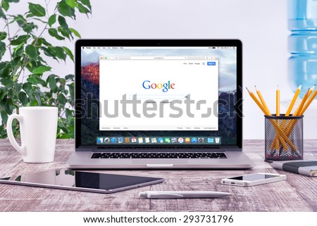 Open Apple 15 inch MacBook Pro Retina with an open tab in Safari which shows Google search web page with ipad and iphone on the wooden office desk workplace. Varna, Bulgaria - May 29, 2015.