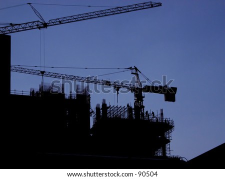 Silhouette of building site with 2 cranes and men climbing scaffolding.