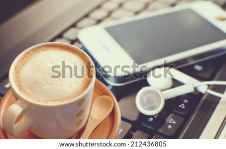 Coffee cup with smart phone and headphones on laptop, soft tone.