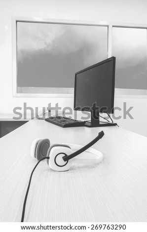 white headphone with computer set and telephone on wood table in office, with blue sky background, black and white tone.