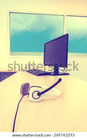 white headphone with computer set and telephone on wood table in office, with blue sky background, vintage tone