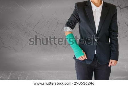 Injured businesswoman with green cast on hand and arm on blurred abstract background