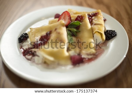 Crepes with strawberries and blackberries, served in white plate with marmalade. Filled with white cheese. Sweet dessert.