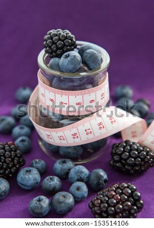 Diet meal. Blackberry and blueberry  in a glass jar with measure tape on the purple background