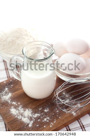 Baking ingredients with milk, eggs, whisk and flour on the table