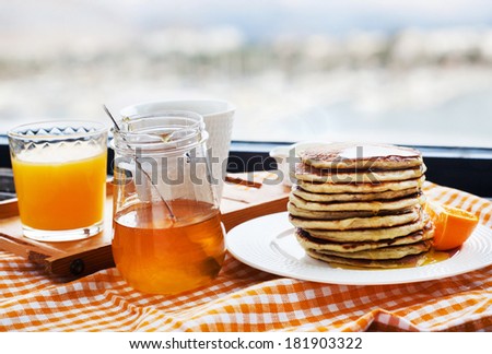 Breakfast with pancakes, coffee, honey and juice on table at the window