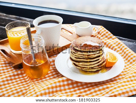 Breakfast with pancakes, coffee, honey and juice on table at the window