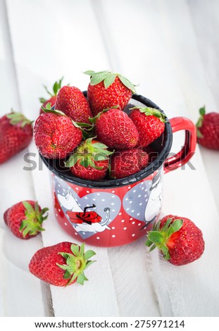 Fresh strawberries  in a red enamelled tin mug on white wooden table