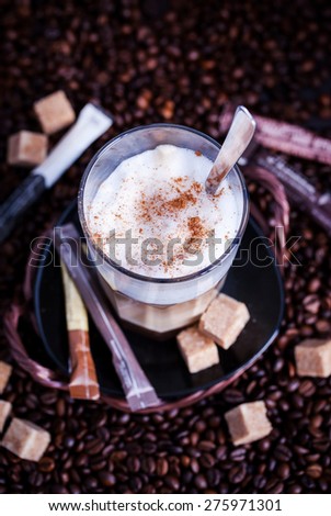 Glass of fresh hot tasty latte macchiato on coffee beans and sugar background, dark style