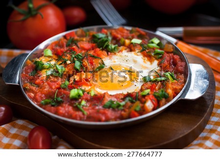 Shakshuka - fried eggs with tomatoes, onion, pepper and spices in iron pan, dark style