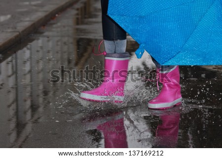 Person with pink boots and blue umbrella splashing in the puddle