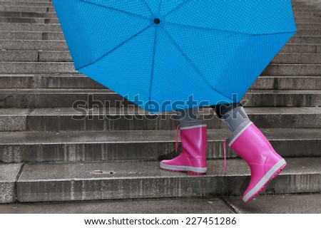 Person with pink boots and blue umbrella walking up the stairs
