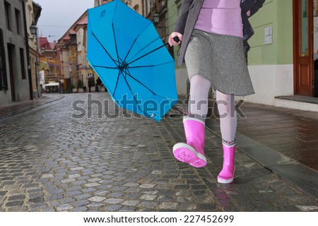 Woman with a blue umbrella in pink boots dancing on the street in the rain