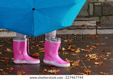 Person with pink boots and blue umbrella standing in standing on a wet sidewalk