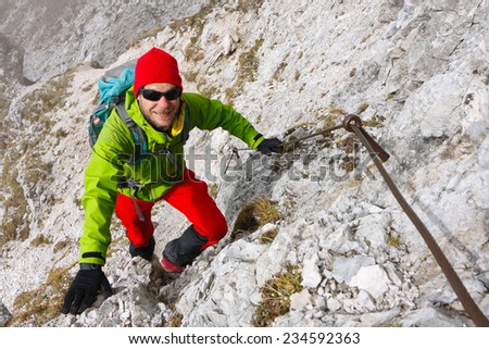 Mountaineer climbing the rocky Kepa mountain wall on a path secured by pins and cables, Slovenia