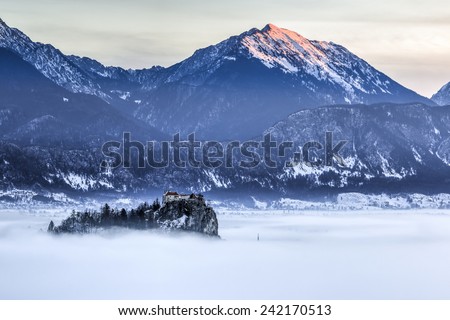 Bled Castle raising above the fog with Karavanke mountains lit by the raising sun in the background, Slovenia