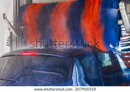 Car wash, black car in automatic car wash, rotating red and blue brushe. Washing vehicle.