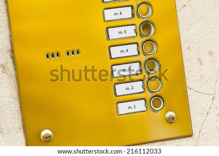 Metal keypad of intercom with numbers, part of home phone on the wall.