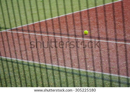A tennis ball on the tennis court, the view through the fence.