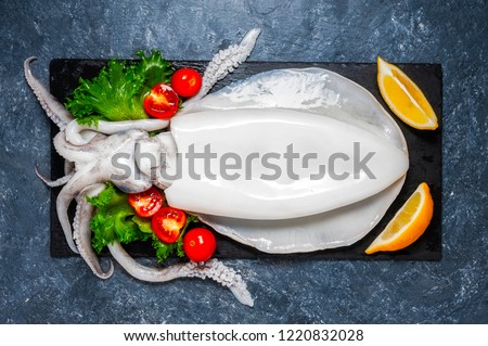 Fresh raw cuttlefish. Raw squid over black slate plate with ice, slices of lemon, tomato. Top view and copy space for your text.