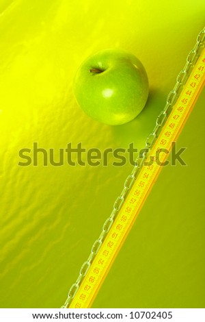 The green apple lays on a gold background with tape measure and a chain