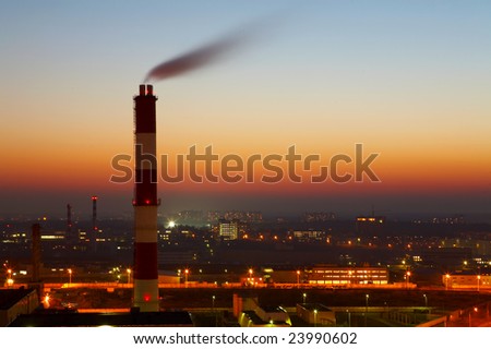 The image of a smoking factory pipe against a sunset