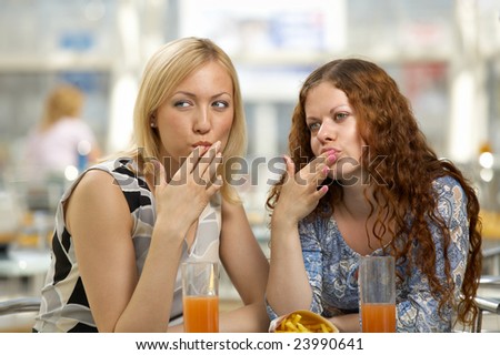 Girl-friends eat snack in cafe and lick fingers
