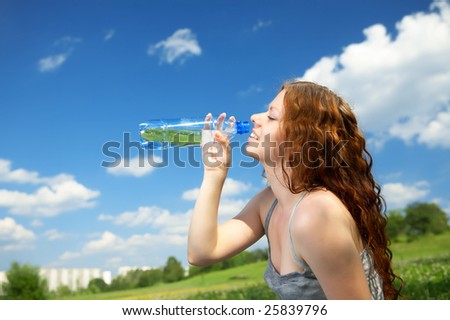The woman in a profile drinks water from a bottle in park