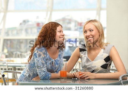 Two girls in cafe confidentially look against each other and smile