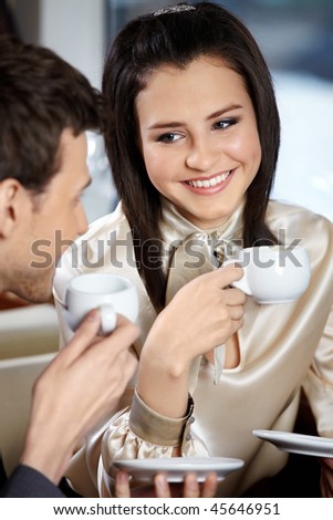 Man and woman in cafe drink coffee and smile, looking against each other