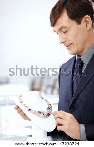 The man in a suit considers a necklace in shop