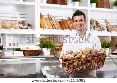 The seller in shop holds a basket with rolls