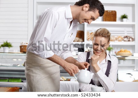 The waiter pours tea to the attractive girl in cafe
