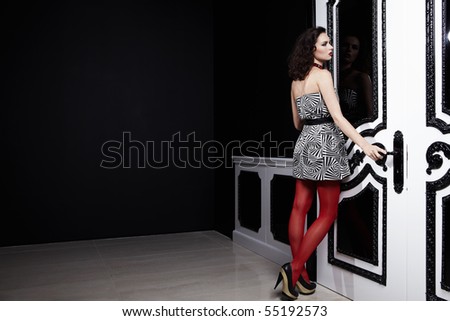 The girl in a dress and red stockings costs at a black-and-white door