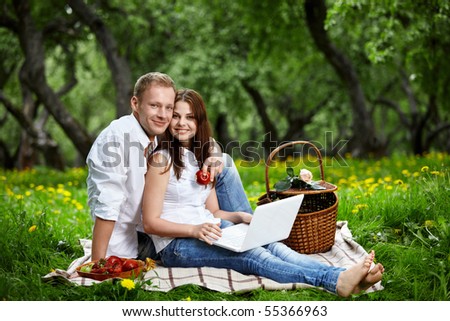 Happy couple on picnic with the laptop in wood