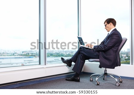 Chief works with a laptop in the office on the background of a large window