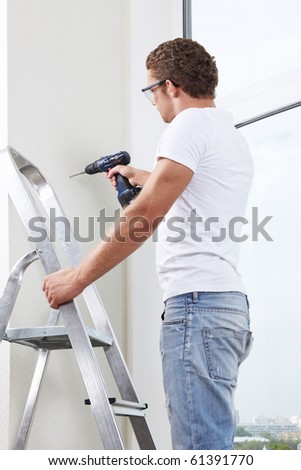 A young man on a ladder working with a drill