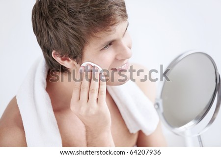 Young man rubbing lotion face in the mirror