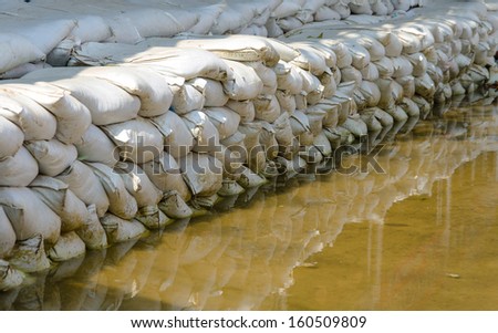 White sandbags for flood defense and it\'s reflection brown water.