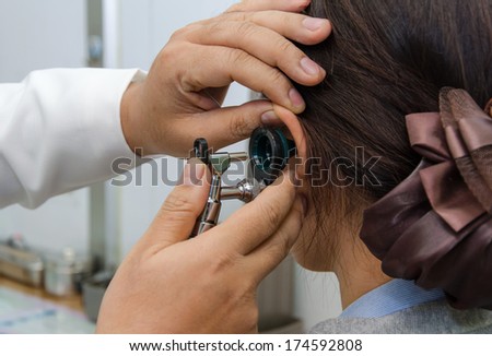 ENT physician checking patient\'s ear using otoscope with an instrument.